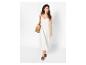Femme en robe longue blanche, sandales marron et sac en paille.