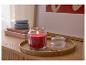 Bougie parfumée rouge dans un pot en verre sur un plateau en bois avec des bijoux.