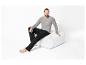 Homme en chemise grise à manches longues et pantalon noir, assis sur un pouf blanc.