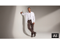 Homme en chemise blanche, pantalon marron et bottes appuyé contre un mur.