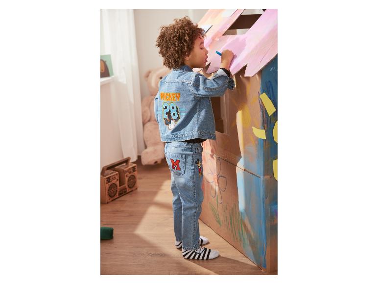 Un enfant vêtu d'un jean et d'une veste en jean Mickey Mouse dessine sur une maison en carton.