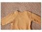 Un haut à manches longues beige clair avec des boutons dans le dos, sur un fond tricoté.