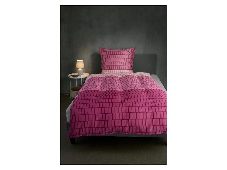 Parure de lit rose à motif géométrique sur un lit dans une chambre avec lampe de chevet.