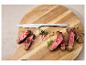Couteau à steak et steak tranché avec herbes et épices sur une planche en bois.