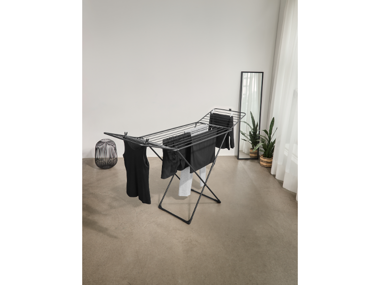 Séchoir à linge noir avec des vêtements sombres dans une pièce lumineuse.