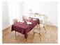 Une nappe bordeaux à motif floral orne une table à manger avec des chaises beige.