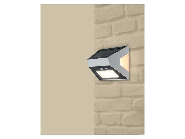 Applique murale solaire avec détecteur de mouvement et deux lumières, fixée sur un mur de briques.