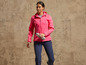 Une femme portant une veste softshell rose et un pantalon bleu tient une bouteille d'eau.