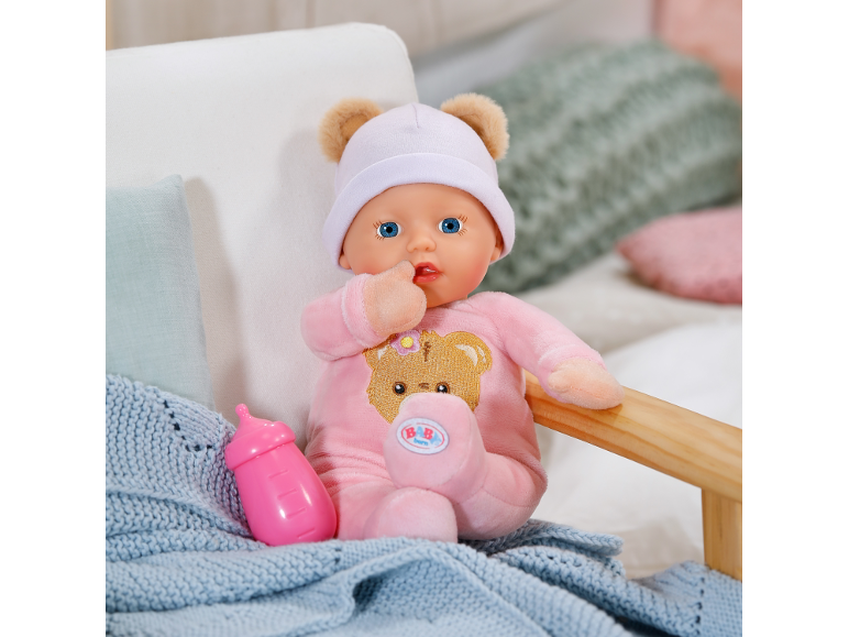 Poupée bébé souple en pyjama rose et bonnet avec oreilles d'ours à côté d'un biberon.