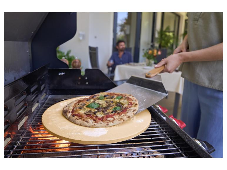 Pizza sur une pierre à pizza sur un grill, avec une personne utilisant une pelle à pizza.