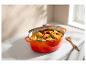 Cocotte en fonte orange remplie de poulet rôti et de légumes sur un comptoir de cuisine.