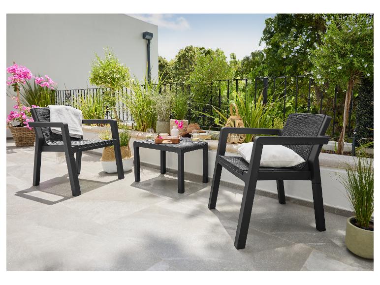 Ensemble de mobilier de jardin: deux fauteuils noirs et une table basse sur une terrasse verdoyante.