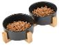 Deux gamelles noires pour animaux de compagnie remplies de croquettes, sur des supports en bois.