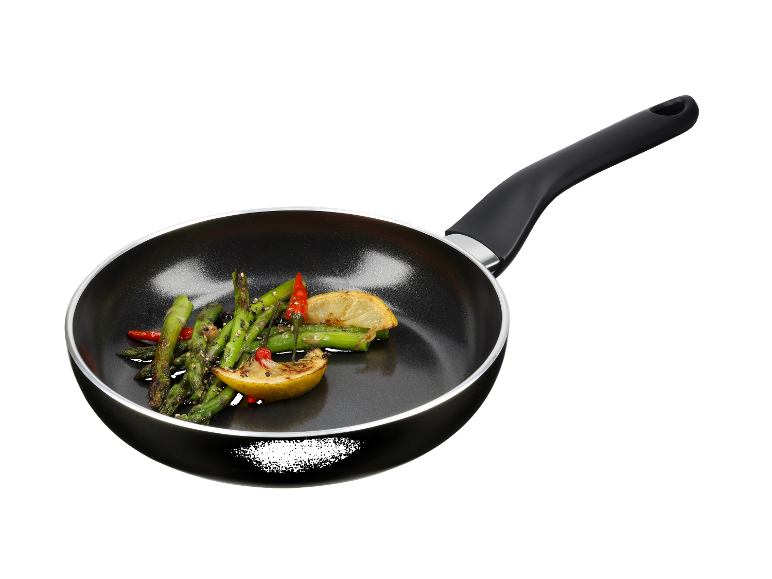 Une poêle noire avec des asperges sautées, du citron et du piment.