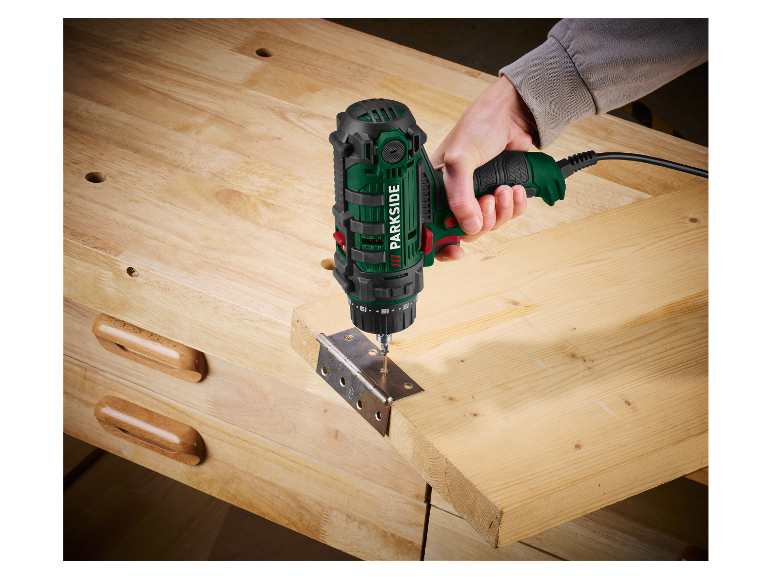 Une personne utilise une perceuse Parkside pour fixer une charnière sur une planche de bois.
