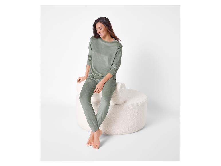Femme en pyjama de velours vert à pois, assise sur un pouf blanc.