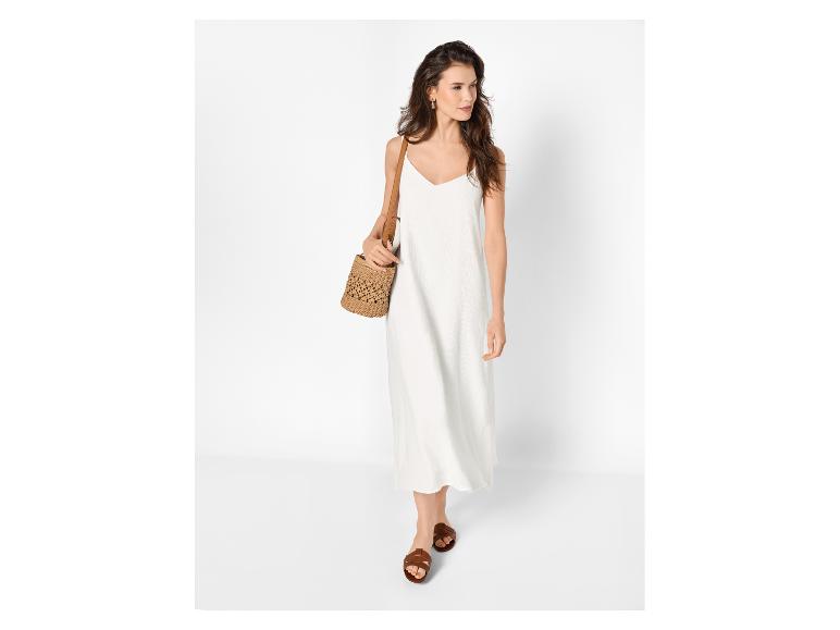 Femme en robe longue blanche, sandales marron et sac en paille.