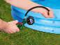 Personne gonflant une piscine gonflable bleue avec une pompe à air numérique, affichant une lecture de 4.64.