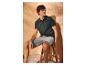 Homme en polo foncé et short clair, assis sur un tabouret en bois.