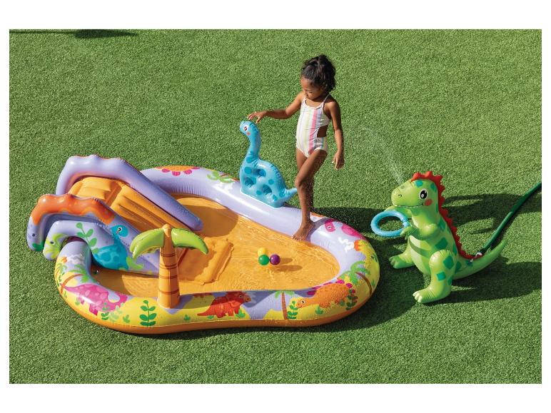 Piscine gonflable thème dinosaures avec toboggan et arroseur, avec une petite fille qui joue.