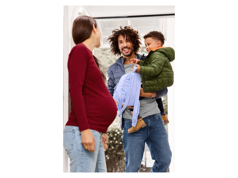 Une femme enceinte accueille un homme avec un enfant et un sac à dos.
