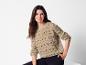 Une femme porte un pull en maille beige avec des détails ajourés.