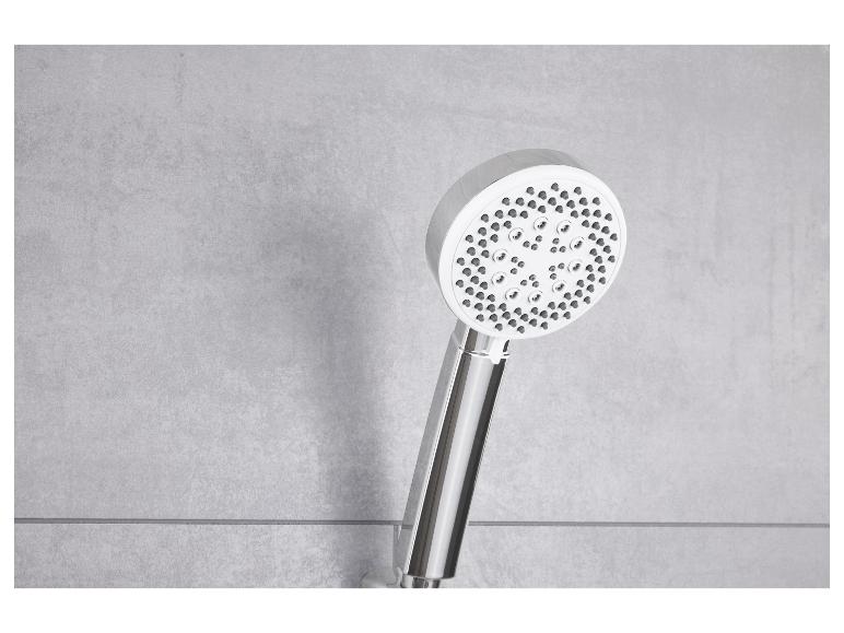 Une pomme de douche chromée avec de multiples buses de pulvérisation devant un mur de carreaux gris.