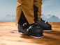 Des chaussures de ski noires avec un accent blanc sur un sol en bois.