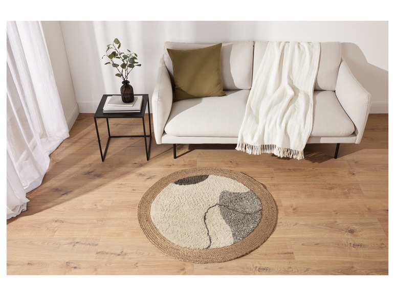 Un tapis rond en jute avec un motif abstrait devant un canapé blanc avec une couverture blanche.