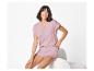 Femme souriante en pyjama court rose assise sur une chaise blanche.