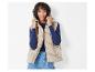 Une femme porte une veste beige, un haut bleu à manches longues et un jean.