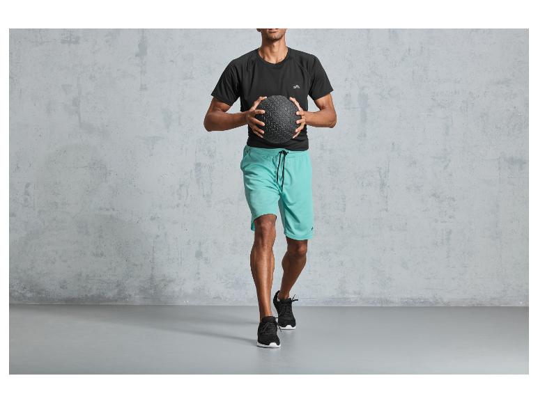 Homme en t-shirt noir et short bleu tenant un ballon de médecine.