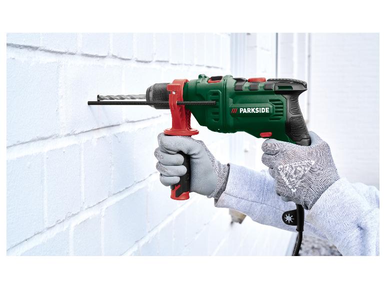 Homme en gants de protection perçant un mur blanc avec une perceuse à percussion.