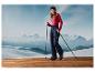 Une femme en tenue de ski avec des bâtons de ski se tient sur une plateforme en bois avec des montagnes en arrière-plan.