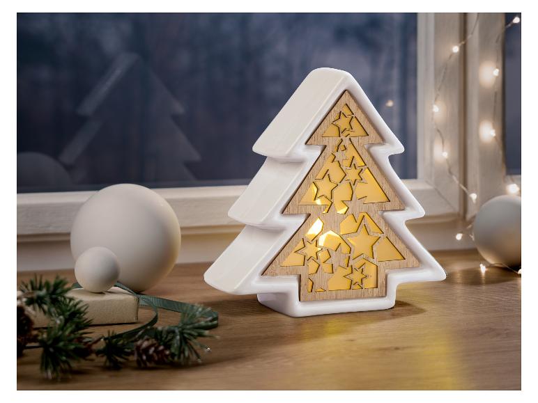 Une lumière d'arbre de Noël en céramique blanche avec des découpes d'étoiles, à côté de sphères décoratives blanches et de verdure festive.