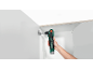 Une perceuse d'angle électrique verte et noire est utilisée pour installer une charnière dans une armoire blanche.
