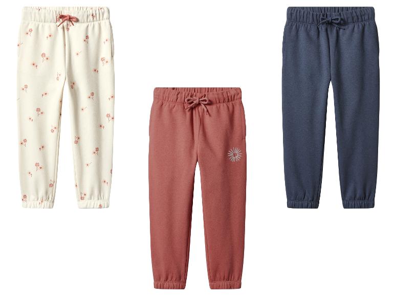 Trois joggings pour enfants : un à fleurs, un rouge brique et un bleu marine.