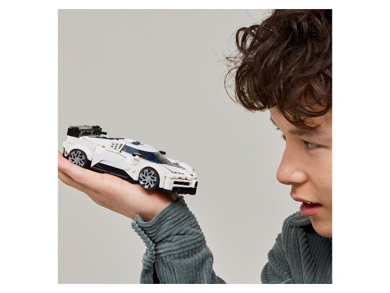 Un jeune homme regarde une voiture de course miniature blanche qu'il tient dans sa main.