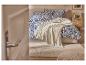 Chambre avec literie florale bleue, couverture claire et table de chevet en bois.