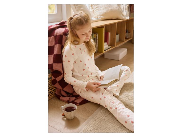 Fille en pyjama à cœurs lisant un livre par terre avec une tasse de thé.