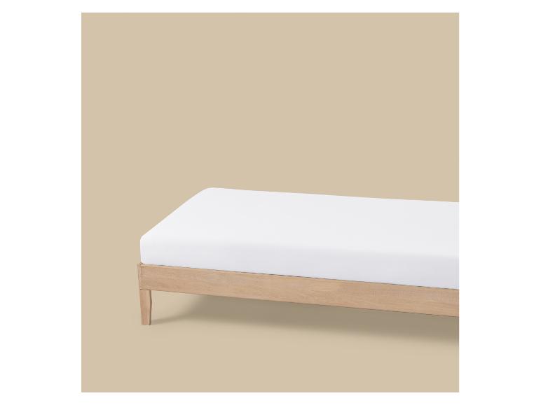 Un matelas blanc sur un cadre de lit en bois clair sur fond beige.
