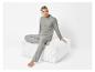 Homme en pantalon et chemise de pyjama gris assis sur un pouf en velours blanc.