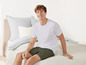 Un homme en t-shirt blanc et short vert assis sur un lit.