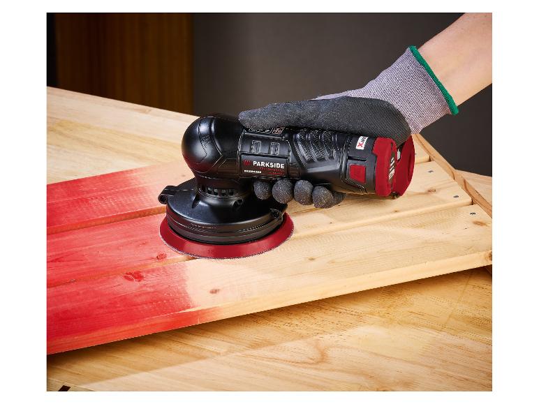 Une personne ponce une planche de bois rouge avec une ponceuse orbitale sans fil.