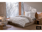 Chambre chaleureuse avec parure de lit d'hiver au motif norvégien devant une fenêtre enneigée.