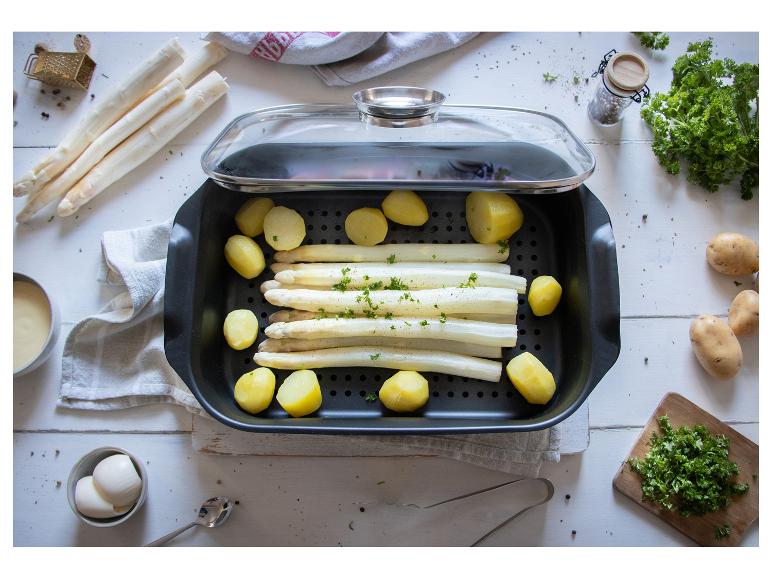 Asperges blanches et pommes de terre dans un plat de cuisson avec couvercle en verre, entourées d'ingrédients frais.