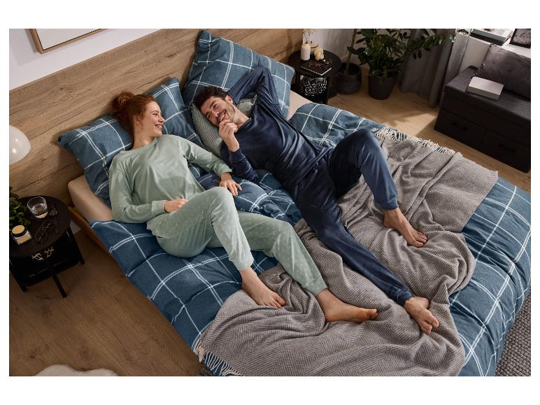 Un couple souriant se détend au lit, portant des pyjamas assortis, avec une parure de lit à carreaux.