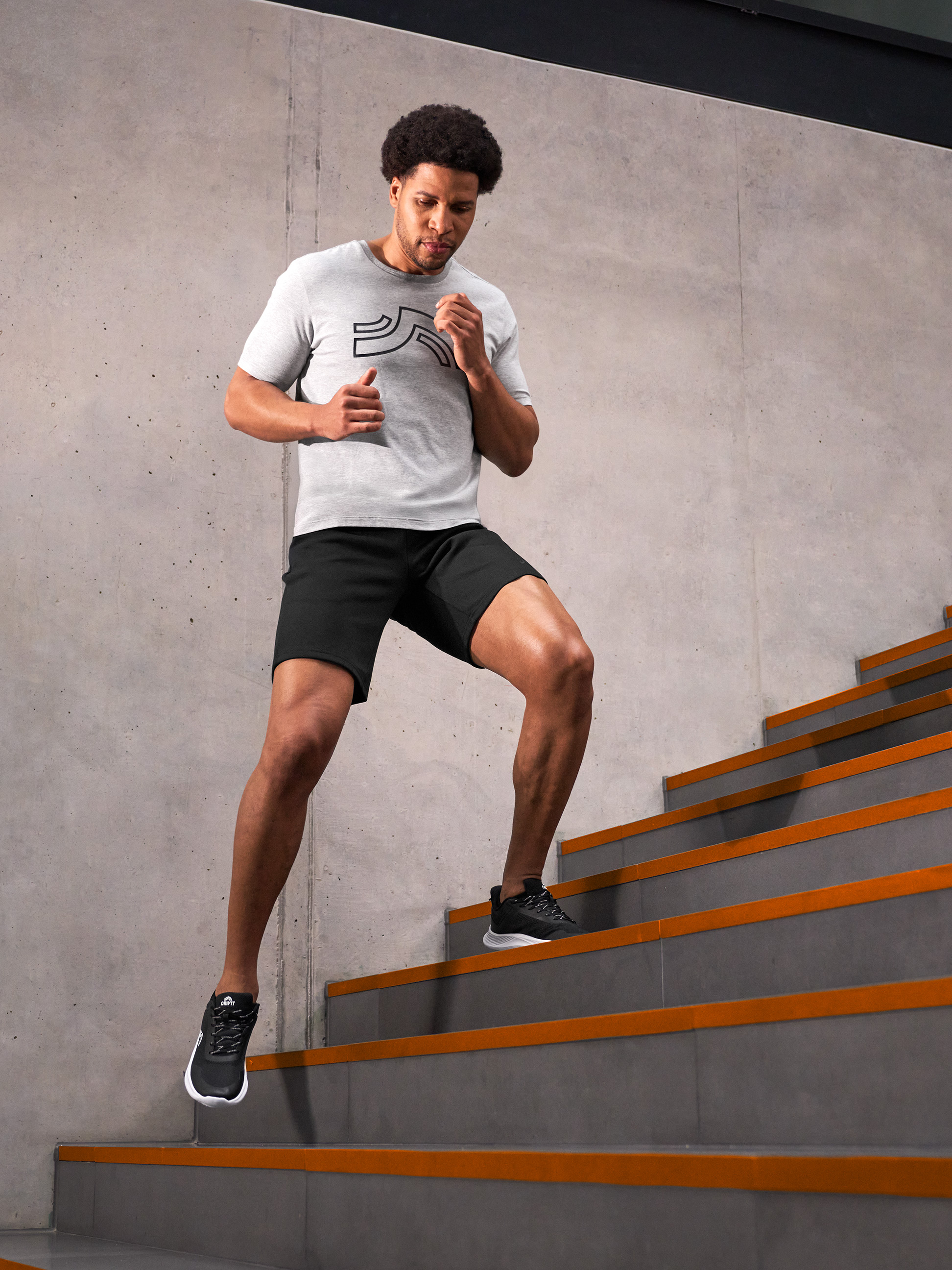 Homme en t-shirt gris et short noir montant des escaliers en béton avec des bandes oranges.