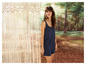 Une femme en combinaison bleue devant un rideau en macramé.