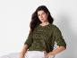 Une femme porte un pull vert avec des détails ajourés et un pantalon blanc.